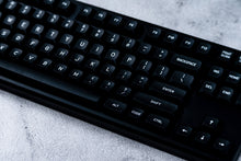 Load image into Gallery viewer, GMK MTNU WoB black keycaps on white 65% keyboard, angled front view on dark wood