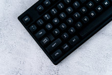 Load image into Gallery viewer, GMK MTNU WoB black keycaps on white keyboard, low angle side profile on dark wood surface