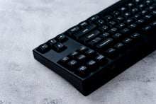 Load image into Gallery viewer, GMK MTNU WoB black keycaps on white keyboard, close-up of left modifiers showing MTNU profile on dark wood