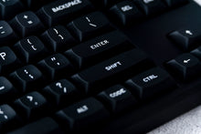 Load image into Gallery viewer, GMK MTNU WoB black keycaps on white keyboard, angled left side view with plant blur on dark wood