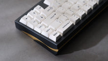 Load image into Gallery viewer, GMK CYL BoW white keycaps on dark navy keyboard with gold accent weight, close-up angled view