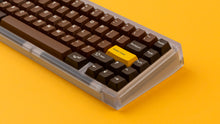 Load image into Gallery viewer, GMK CYL Chocolatier keycaps on clear transparent 65% keyboard against orange background, close-up of left side