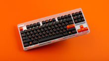 Load image into Gallery viewer, GMK CYL Kaiju R3 dark base keycaps on clear TKL keyboard, angled top-down on orange background