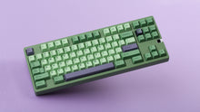 Load image into Gallery viewer, GMK CYL Zooted keycaps on green 1800 compact keyboard, angled top-down shot with purple accent spacebar and modifier keys against a lavender background