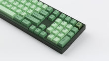 Load image into Gallery viewer, GMK CYL Zooted keycaps on dark green full-size keyboard, close-up of right side showing numpad, navigation cluster, and leaf novelty accent keycap on white surface