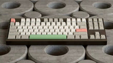Load image into Gallery viewer, Render of GMK CYL Classic Beige keycaps with pink and green accents on dark bronze TKL keyboard, angled front view on concrete background