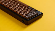 Load image into Gallery viewer, Render of GMK CYL Chocolatier keycaps on a silver aluminum keyboard, side angle view with golden accents